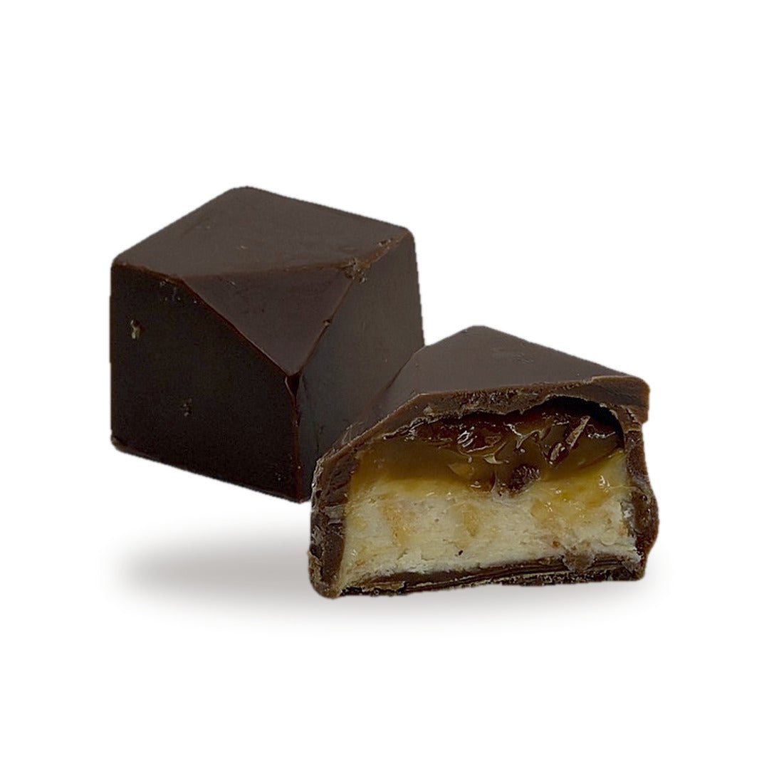 A Baklava Caramel cut open, showing the layered pastry base, caramel and cashew inside the milk chocolate