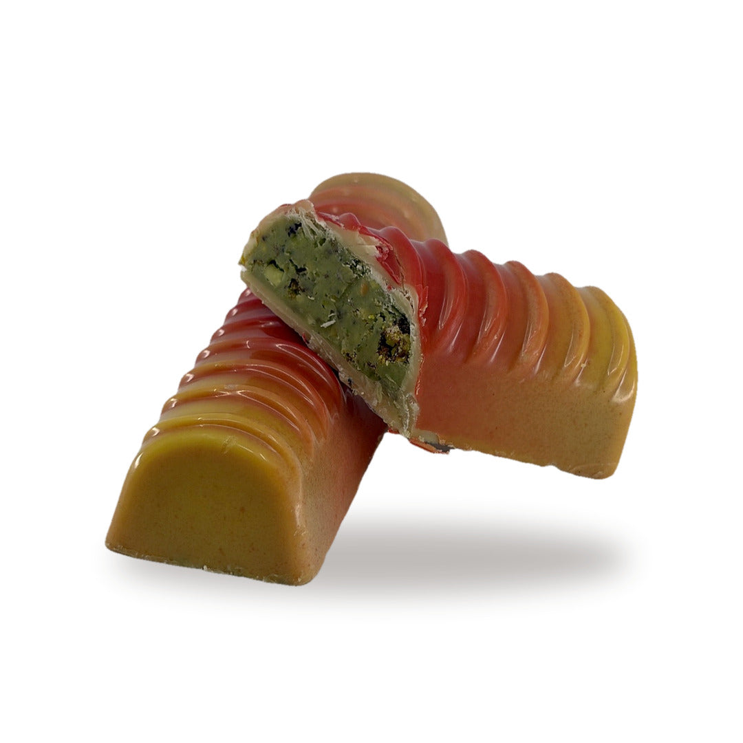A Pistachio Crunch Log cut open, showing the green pistachio filling inside the colored white chocolate shell