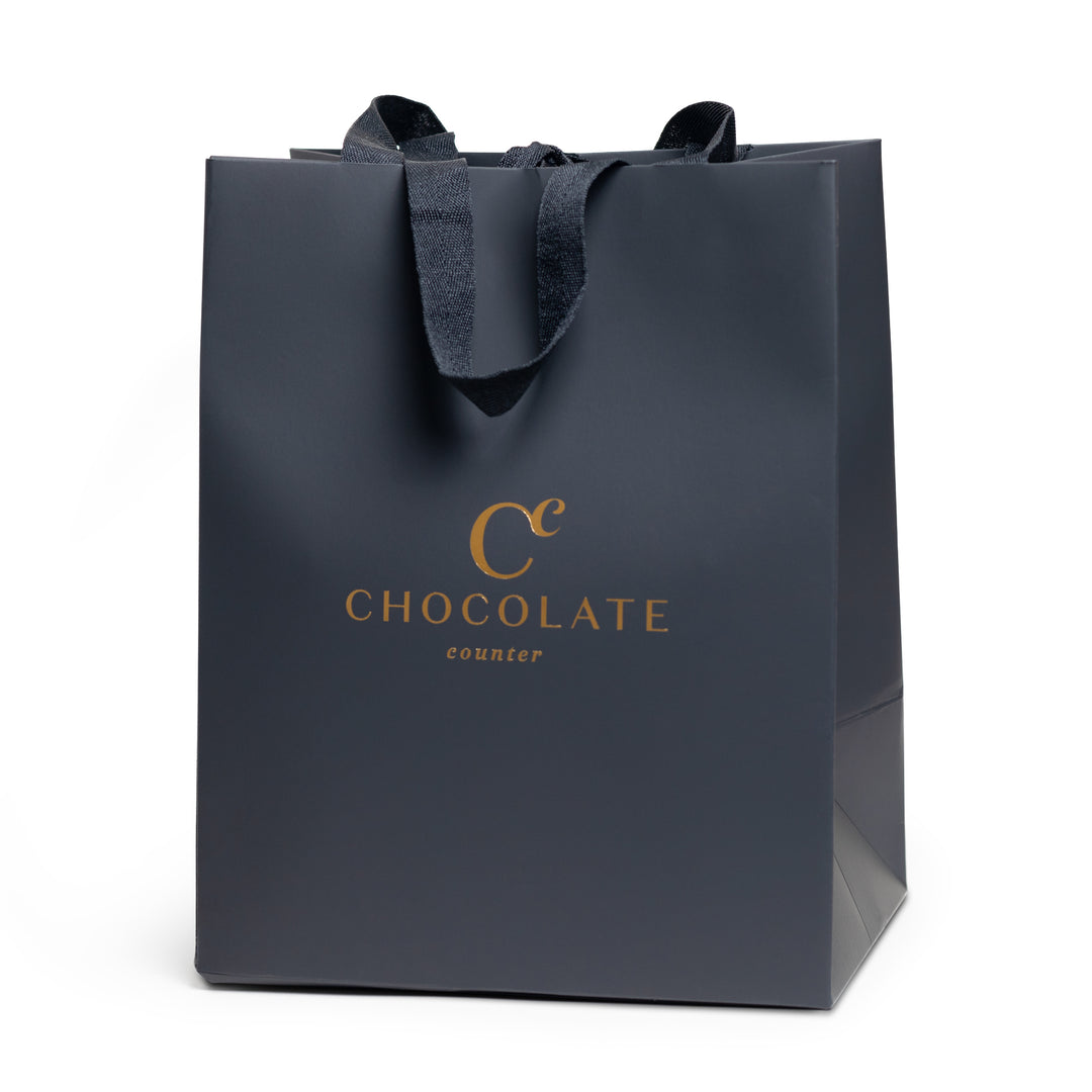 Matte black gift bag with gold Chocolate Counter logo and satin ribbon handles