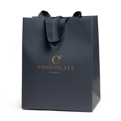 Matte black gift bag with gold Chocolate Counter logo and satin ribbon handles